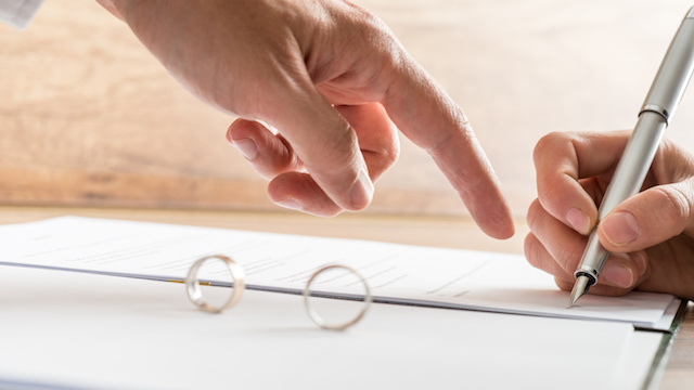 Male hand pointing to a divorce paper on which a woman is busy writing with a pen in a close up conceptual view.